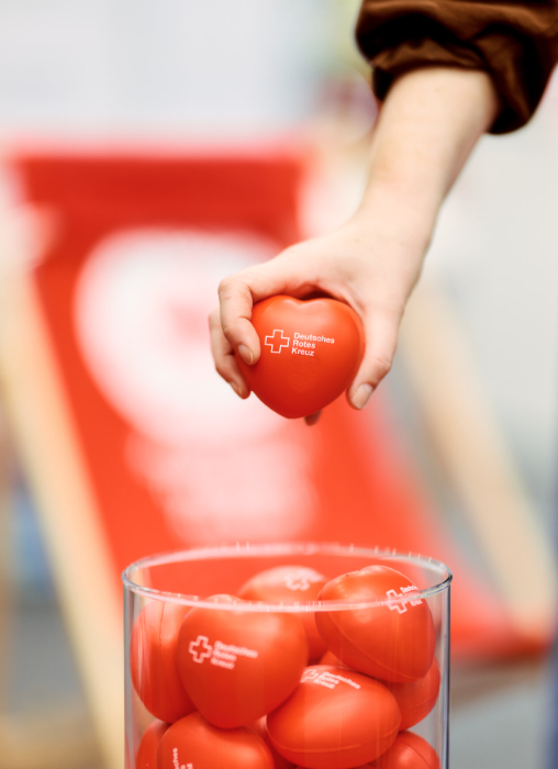 Hand hält ein rotes Herz mit DRK-Logo